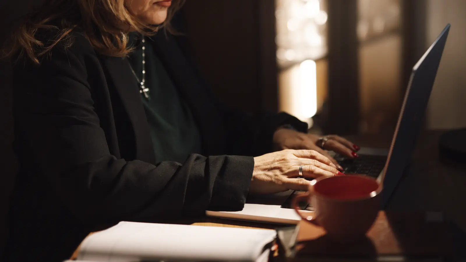 A woman working on a laptop at a desk in warm evening light