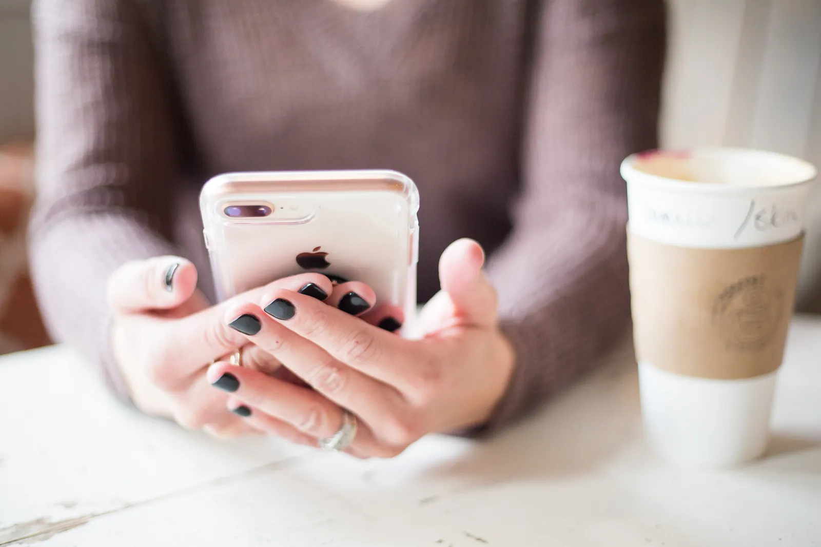 Hands holding a phone beside a coffee cup on a white table