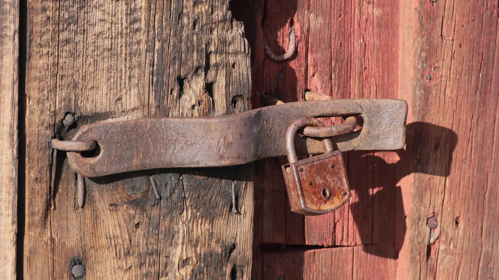 A red padlock on a weathered wooden door