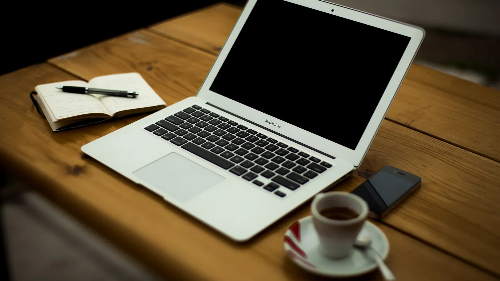 A laptop, notebook and coffee on a wooden desk