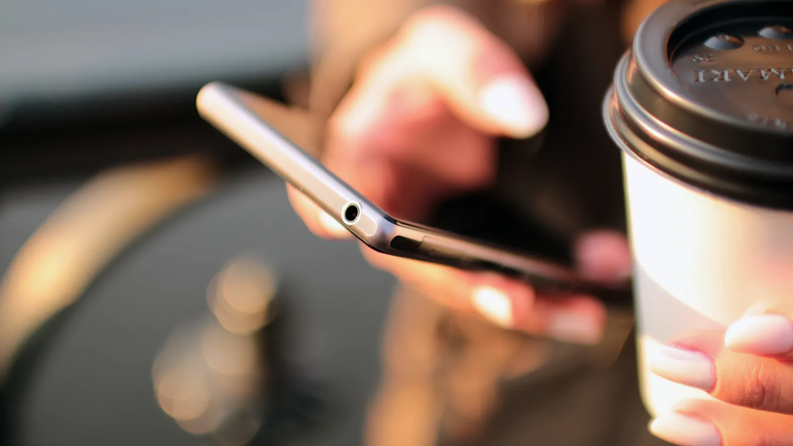 A person holding a smartphone and a takeaway coffee