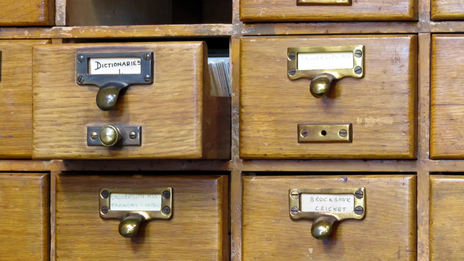 Rows of wooden library card catalogue drawers with brass handles