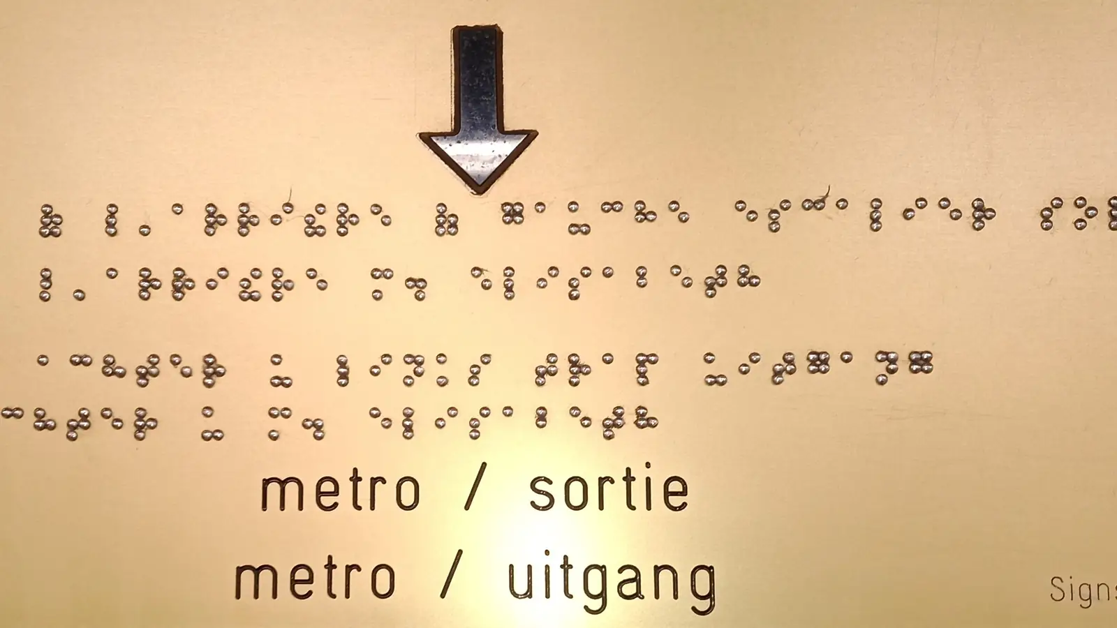 A metro station sign with raised braille dots above the printed words