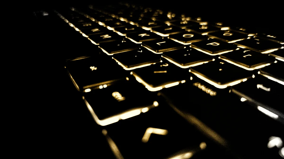 A laptop keyboard lit gold from below in a dark room, seen at a low angle