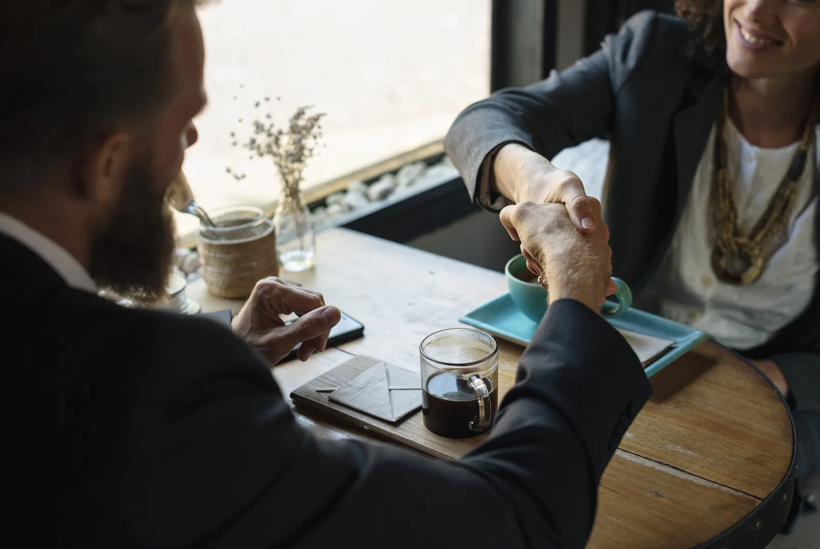 Two people shaking hands across a coffee shop table