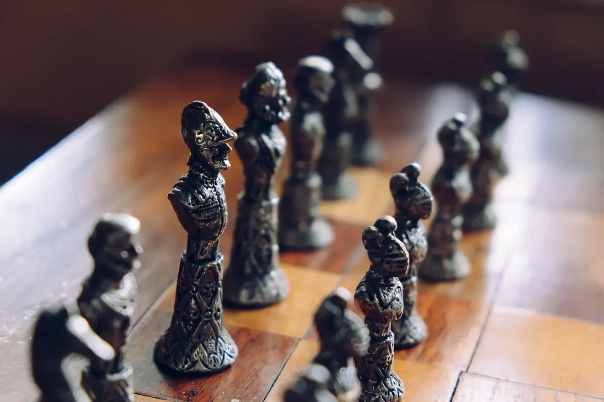 Dark metal chess pieces lined up on a polished wooden board