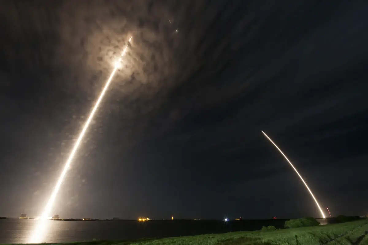 Two bright rocket launch trails arcing across a dark night sky