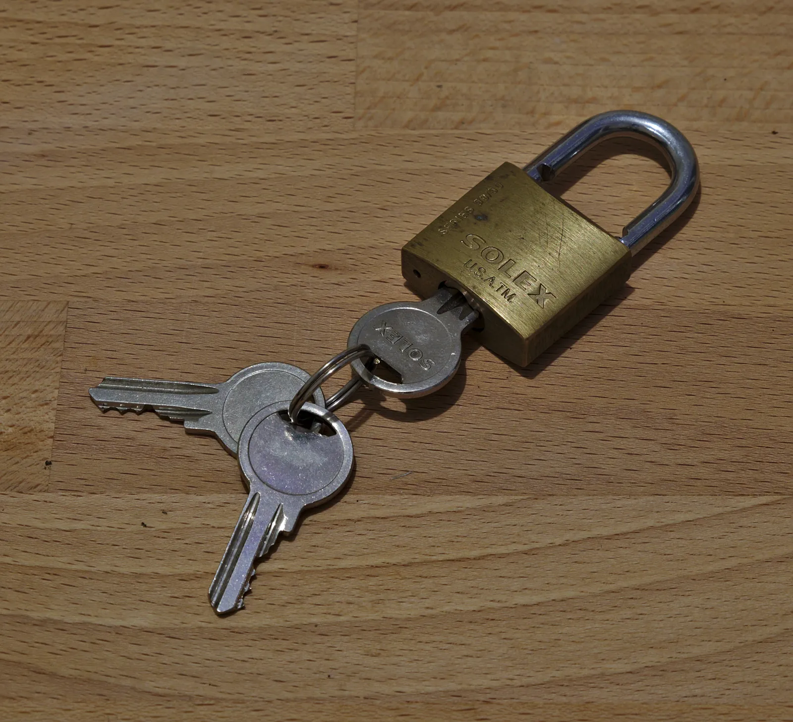 A brass padlock with its keys on a wooden table