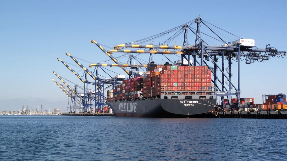 A container ship at berth beside blue and yellow gantry cranes under a clear sky